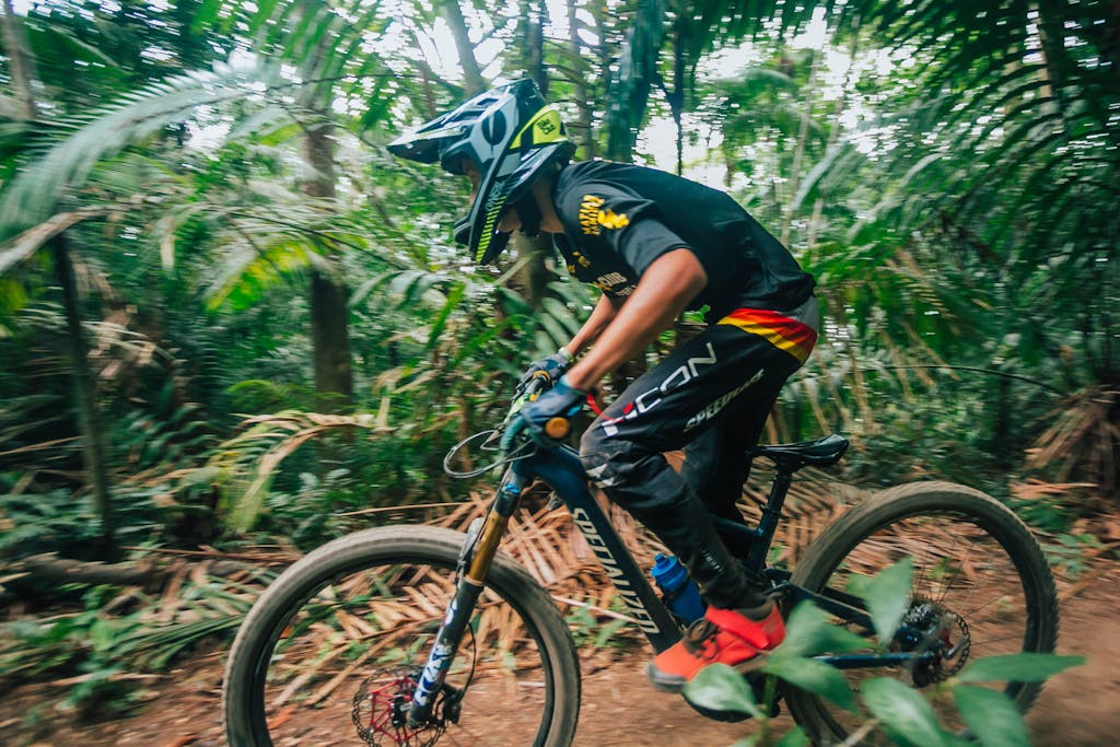 A mountain biker rapidly navigates wooded trails, wearing protective gear and focused on the path ahead.