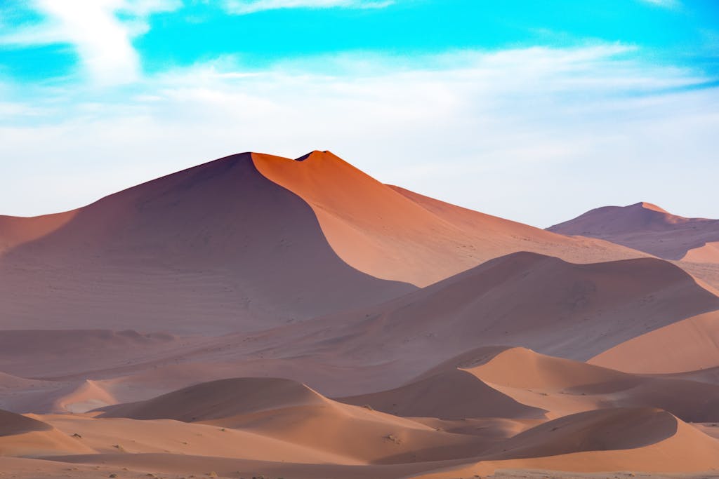 Capture the serene beauty of Namibian sand dunes under a vibrant sky. Perfect for desert-themed designs.