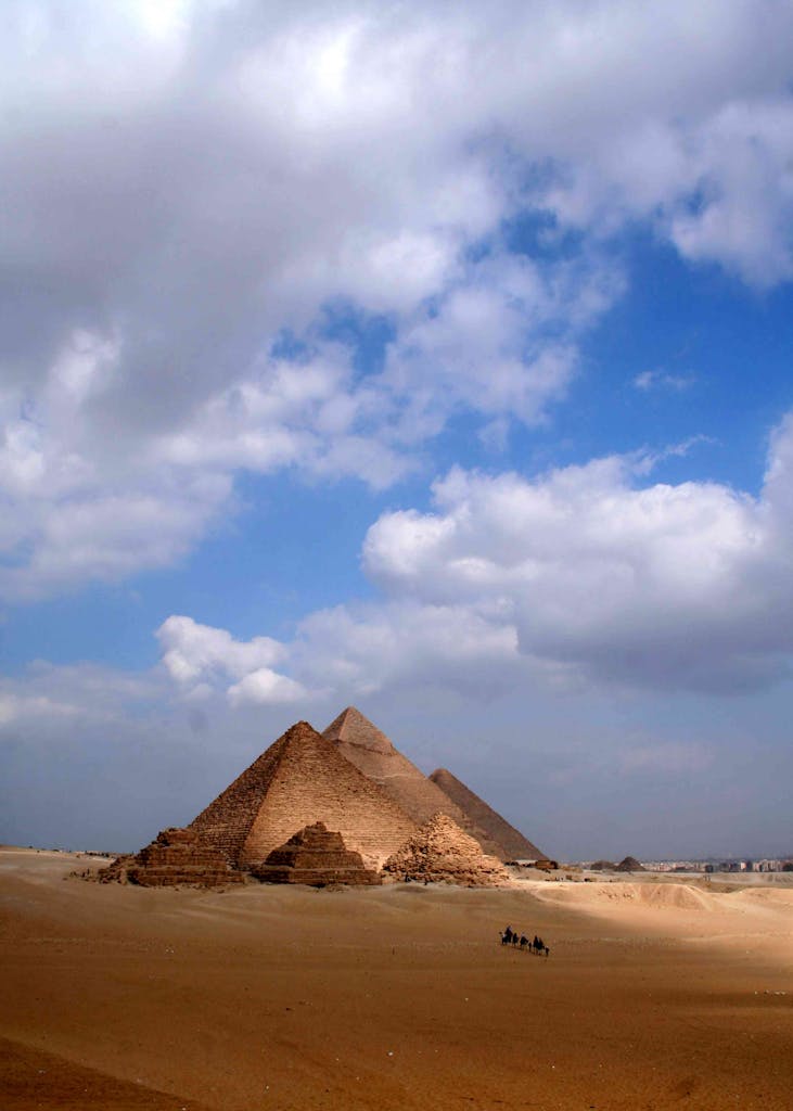 The iconic Pyramids of Giza stand majestically under a bright blue sky with scattered clouds.