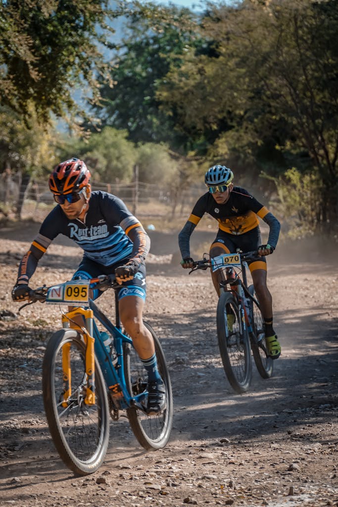 Two cyclists race fiercely on a dusty mountain trail under clear skies.