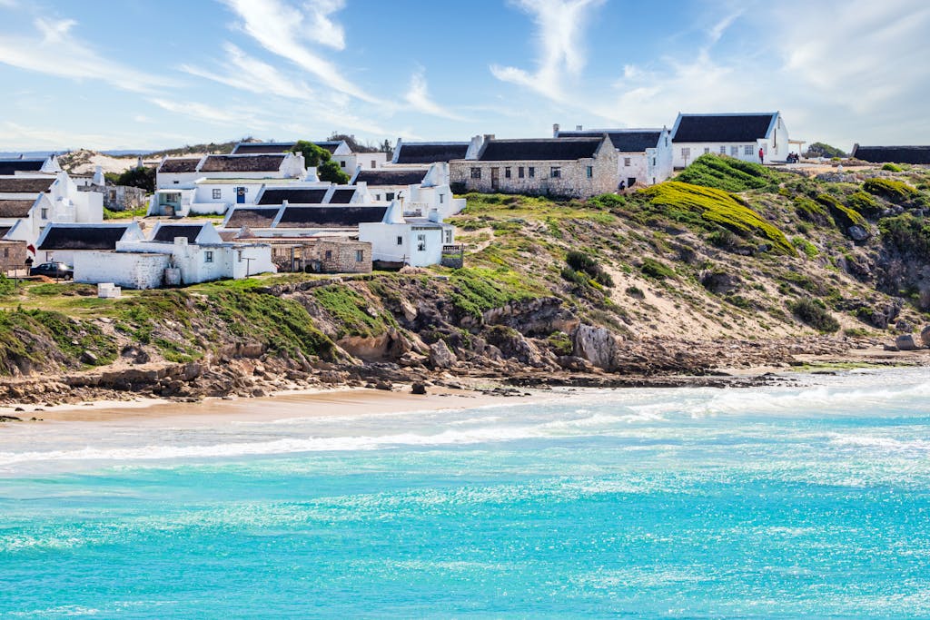 Charming seaside village of Arniston in South Africa with whitewashed cottages overlooking the turquoise ocean.