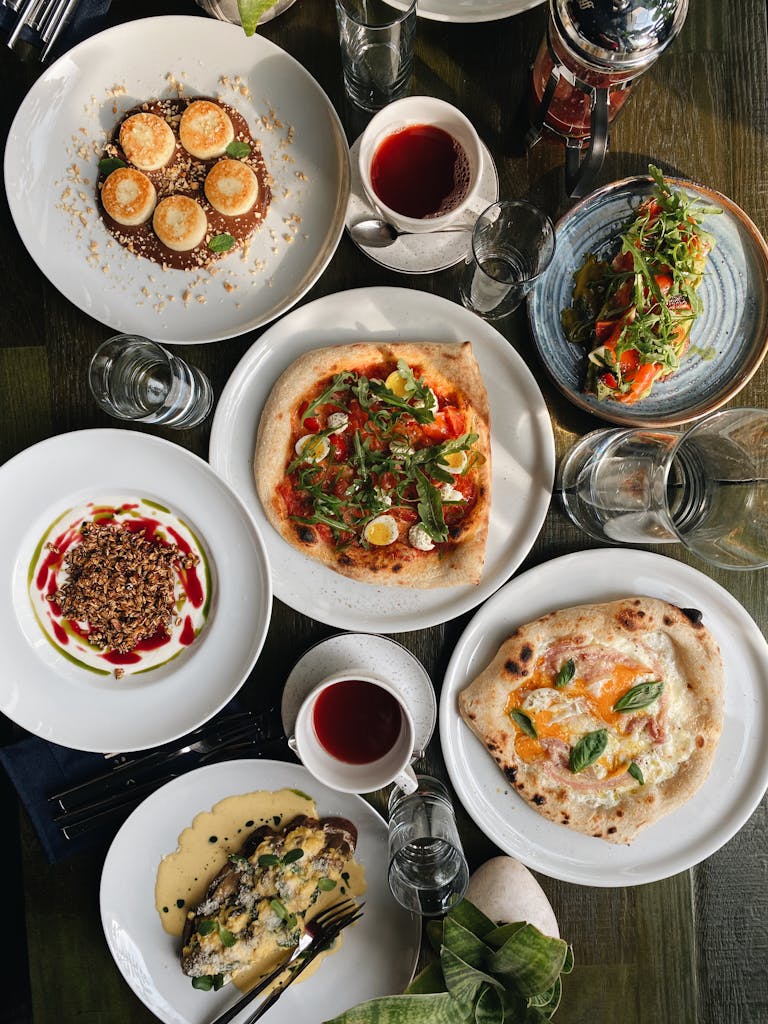 Flat lay of diverse Italian dishes including pizza, salads, and desserts on a dining table.