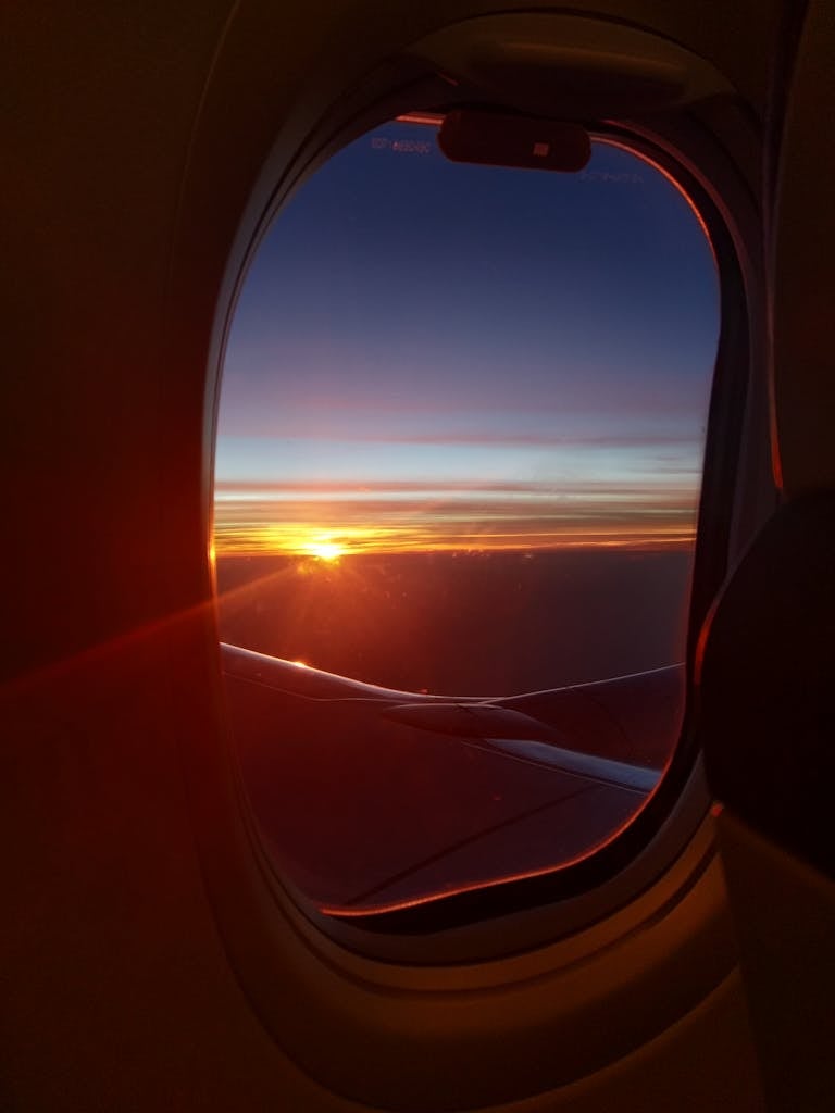Airplane window view showcasing a vibrant sunset over the clouds, highlighting the beauty of air travel.