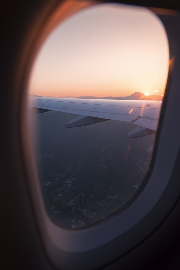 Airplane wing view through window during sunset, capturing a serene sky and landscape below.