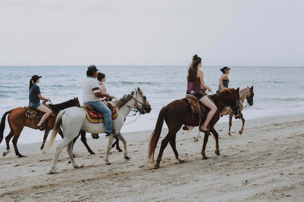 Group of people enjoying horseback riding along Bucerías beach, Mexico, against ocean waves.