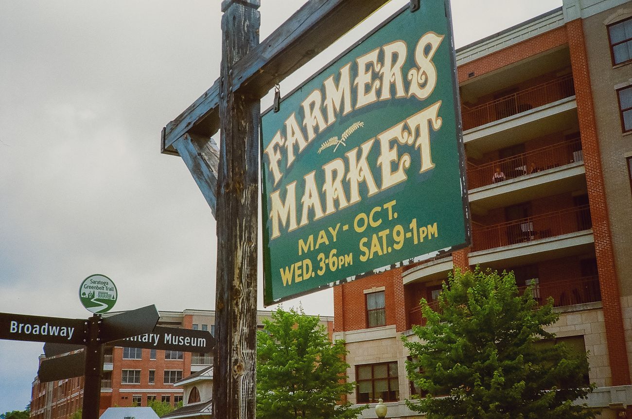 Farmers Market sign in Saratoga Springs with nearby urban buildings and directional signs.